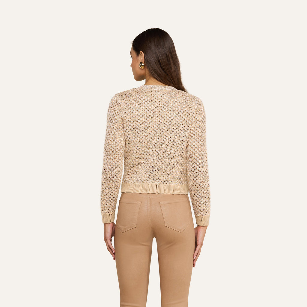 A woman with long brown hair and gold earrings stands with her back to the camera, wearing the Blanca Sequin Cardigan and high-waisted tan pants against a neutral background.