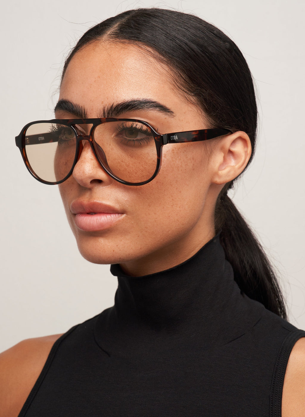 Otra Eyewear - Stevie Tortoiseshell/Brown - Model wearing the Stevie sunglasses featuring a classic oversized aviator silhouette in a tortoiseshell frame, paired with smooth light brown lenses in a three-quarter side portrait shot against a light grey background. A laid-back statement that balances warmth and cool, offering retro charm with a modern edge that is timeless, effortless, and made to stand out.