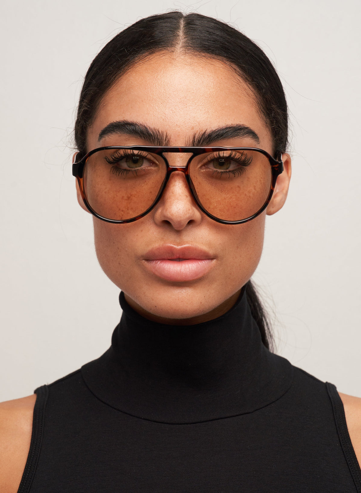 Otra Eyewear - Stevie Tortoiseshell/Brown - Model wearing the Stevie sunglasses featuring a classic oversized aviator silhouette in a tortoiseshell frame, paired with smooth light brown lenses in a front portrait shot against a light grey background. A laid-back statement that balances warmth and cool, offering retro charm with a modern edge that is timeless, effortless, and made to stand out.
